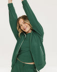 A woman wearing a green long-sleeve jacket with white stripes on the sleeves and matching green pants, standing against a white background.