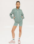 A woman is wearing a long sleeve jacket and shorts with a green and white checkered pattern.