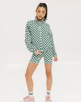 A woman is wearing a long sleeve jacket and shorts with a green and white checkered pattern.