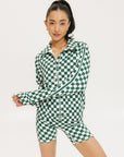 A woman is wearing a long sleeve jacket and shorts with a green and white checkered pattern.