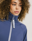 A woman is wearing a blue jacket with a white zipper and green stripes on the sleeves and pants. The jacket has a collared neckline.