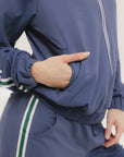 A woman is wearing a blue jacket with a white zipper and green stripes on the sleeves and pants. The jacket has a collared neckline.