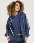 A woman is wearing a blue jacket with a white zipper and green stripes on the sleeves and pants. The jacket has a collared neckline.