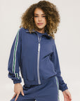 A woman is wearing a blue jacket with a white zipper and green stripes on the sleeves and pants. The jacket has a collared neckline.