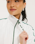 A woman wearing a white long sleeve golf jacket with green accents and a matching visor.