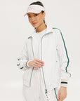 A woman wearing a white long sleeve golf jacket with green accents and a matching visor.