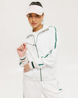 A woman wearing a white long sleeve golf jacket with green accents and a matching visor.