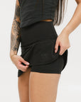 A person wearing a black skirt that reaches mid-thigh, paired with a black top and white socks with black stripes, standing against a white background.