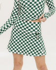 A person wearing a green and white checkered skirt with a matching long-sleeve top and sneakers, standing on a white background.