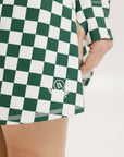 A person wearing a green and white checkered skirt with a matching long-sleeve top and sneakers, standing on a white background.