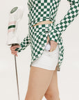 A person wearing a green and white checkered skirt with a matching long-sleeve top and sneakers, standing on a white background.