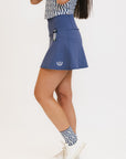 A woman wearing a blue golf skirt with side trim details, paired with a patterned top and white shoes.