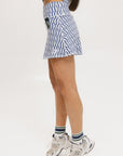 A person wearing a white and blue geometric patterned skirt with side trim details, paired with a matching white top, and light-colored sneakers.