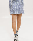 A person wearing a white mid thigh length skirt with side trim details, paired with a white top and patterned socks, standing against a white background.