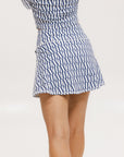 A person wearing a white mid thigh length skirt with side trim details, paired with a white top and patterned socks, standing against a white background.