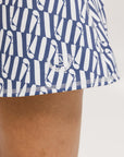A person wearing a white mid thigh length skirt with side trim details, paired with a white top and patterned socks, standing against a white background.
