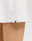 A person wearing a white mid thigh length skirt with side trim details, paired with a white top and patterned socks, standing against a white background.