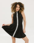 A woman models a black sleeveless dress with a zipper that extends from the top to the bottom. The dress has a relaxed fit and she is wearing it with sneakers.