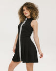 A woman models a black sleeveless dress with a zipper that extends from the top to the bottom. The dress has a relaxed fit and she is wearing it with sneakers.
