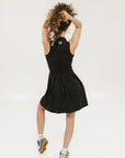 A woman models a black sleeveless dress with a zipper that extends from the top to the bottom. The dress has a relaxed fit and she is wearing it with sneakers.