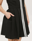 A woman models a black sleeveless dress with a zipper that extends from the top to the bottom. The dress has a relaxed fit and she is wearing it with sneakers.
