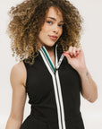 A woman models a black sleeveless dress with a zipper that extends from the top to the bottom. The dress has a relaxed fit and she is wearing it with sneakers.