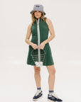 A woman in a green sleeveless knee-length dress with a top-to-bottom zipper, wearing a patterned hat.