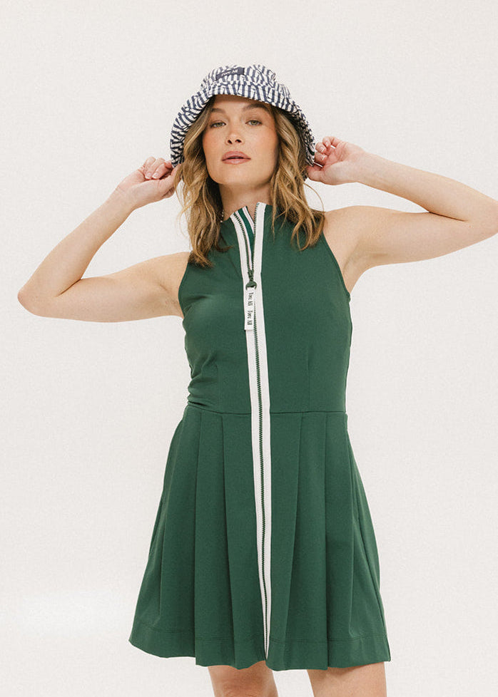 A woman in a green sleeveless knee-length dress with a top-to-bottom zipper, wearing a checkered hat.