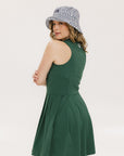 A woman in a green sleeveless knee-length dress with a top-to-bottom zipper, wearing a patterned hat.