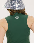 A woman in a green sleeveless knee-length dress with a top-to-bottom zipper, wearing a patterned hat.