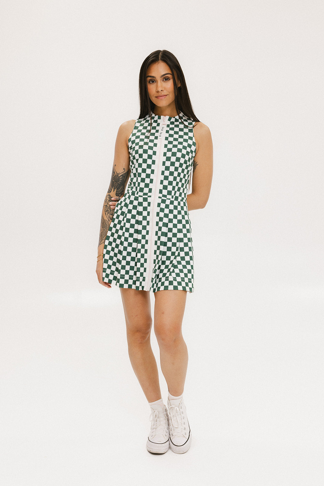 A model wearing a green and white checkered sleeveless dress with a zipper down the front and pockets.