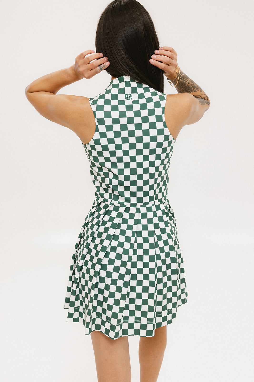 A model wearing a green and white checkered sleeveless dress with a zipper down the front and pockets.