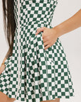 A model wearing a green and white checkered sleeveless dress with a zipper down the front and pockets.