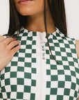 A model wearing a green and white checkered sleeveless dress with a zipper down the front and pockets.