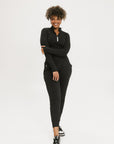 A female model wearing black athletic pants and a long-sleeve black top, standing against a white background.