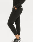 A female model wearing black athletic pants and a long-sleeve black top, standing against a white background.