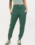A pair of green athletic pants designed for golfing, with a comfortable waistband and a fitted design that enhances the silhouette. The pants are modeled by a woman who is also wearing a checkered top and sneakers.