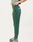 A pair of green athletic pants designed for golfing, with a comfortable waistband and a fitted design that enhances the silhouette. The pants are modeled by a woman who is also wearing a checkered top and sneakers.