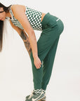 A pair of green athletic pants designed for golfing, with a comfortable waistband and a fitted design that enhances the silhouette. The pants are modeled by a woman who is also wearing a checkered top and sneakers.