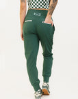 A pair of green athletic pants designed for golfing, with a comfortable waistband and a fitted design that enhances the silhouette. The pants are modeled by a woman who is also wearing a checkered top and sneakers.