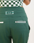 A pair of green athletic pants designed for golfing, with a comfortable waistband and a fitted design that enhances the silhouette. The pants are modeled by a woman who is also wearing a checkered top and sneakers.