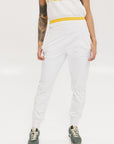 A person wearing white athletic pants and a white t-shirt with yellow details, standing against a white background.