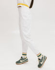 A person wearing white athletic pants and a white t-shirt with yellow details, standing against a white background.