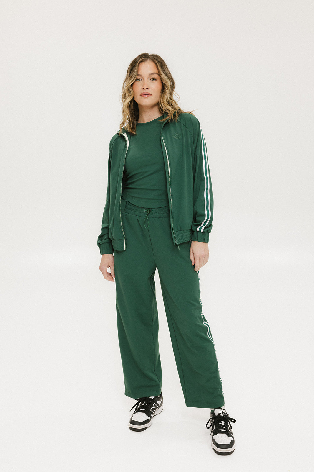 A person standing wearing green Bronson pants with a drawstring waist, green top, and black and white sneakers.