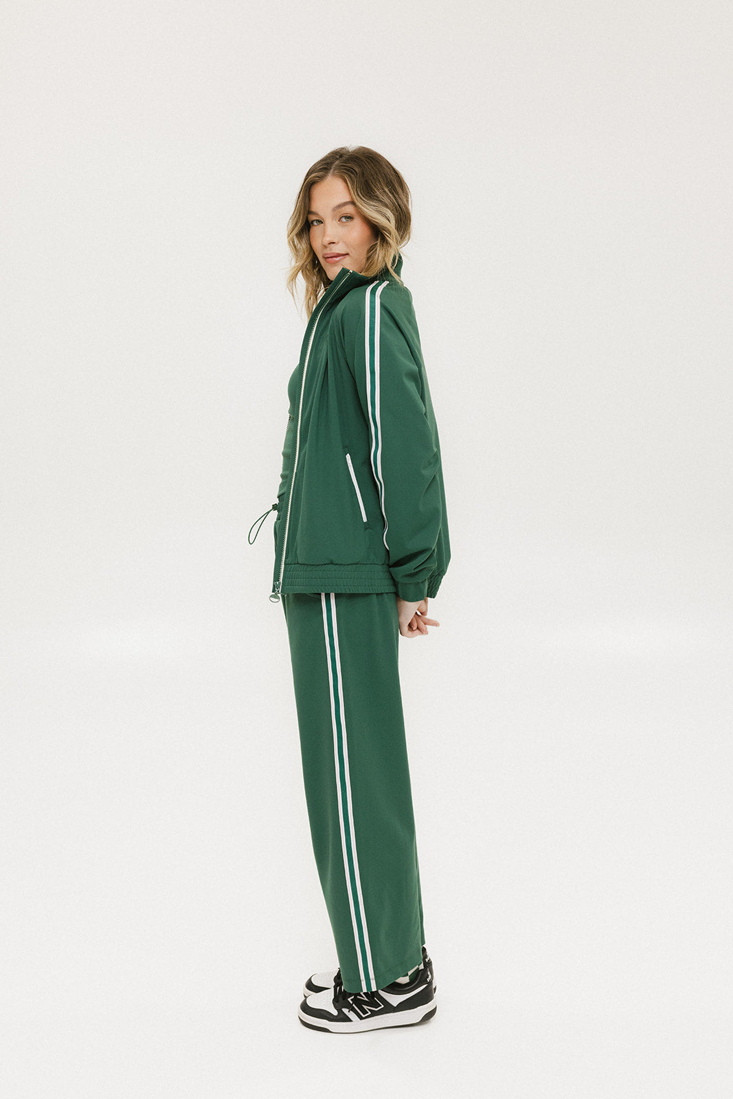 A person standing wearing green Bronson pants with a drawstring waist, green top, and black and white sneakers.