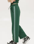 A person standing wearing green Bronson pants with a drawstring waist, green top, and black and white sneakers.