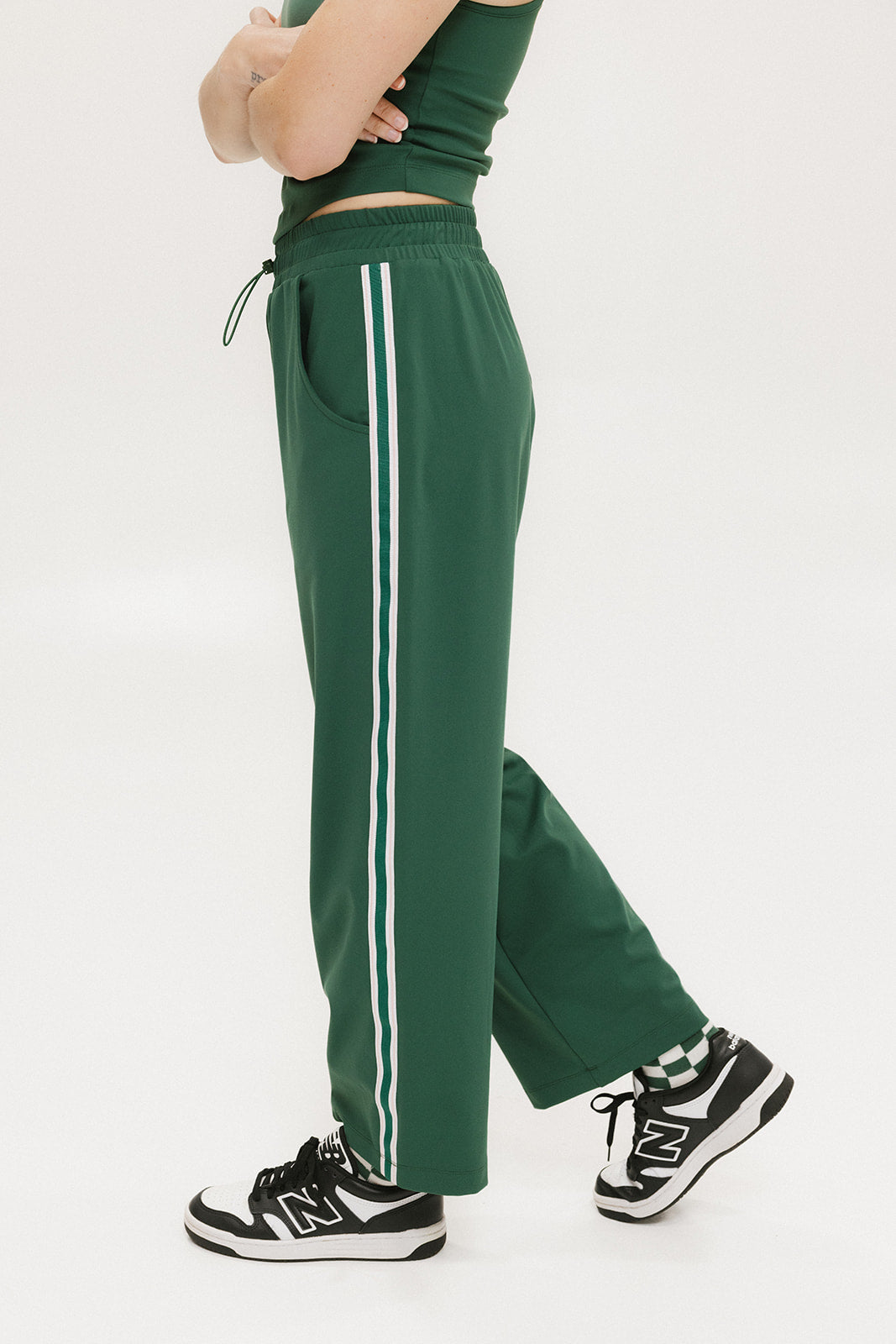 A person standing wearing green Bronson pants with a drawstring waist, green top, and black and white sneakers.