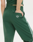 A person standing wearing green Bronson pants with a drawstring waist, green top, and black and white sneakers.