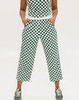 A pair of green checkered pants with a relaxed fit and pockets, worn by a model in a matching checkered top and sneakers.