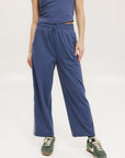 A person standing wearing indigo blue track pants with a drawstring waist and green sneakers.
